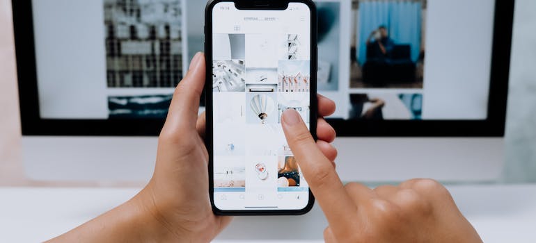 A person holding and using a phone in front of the computer.